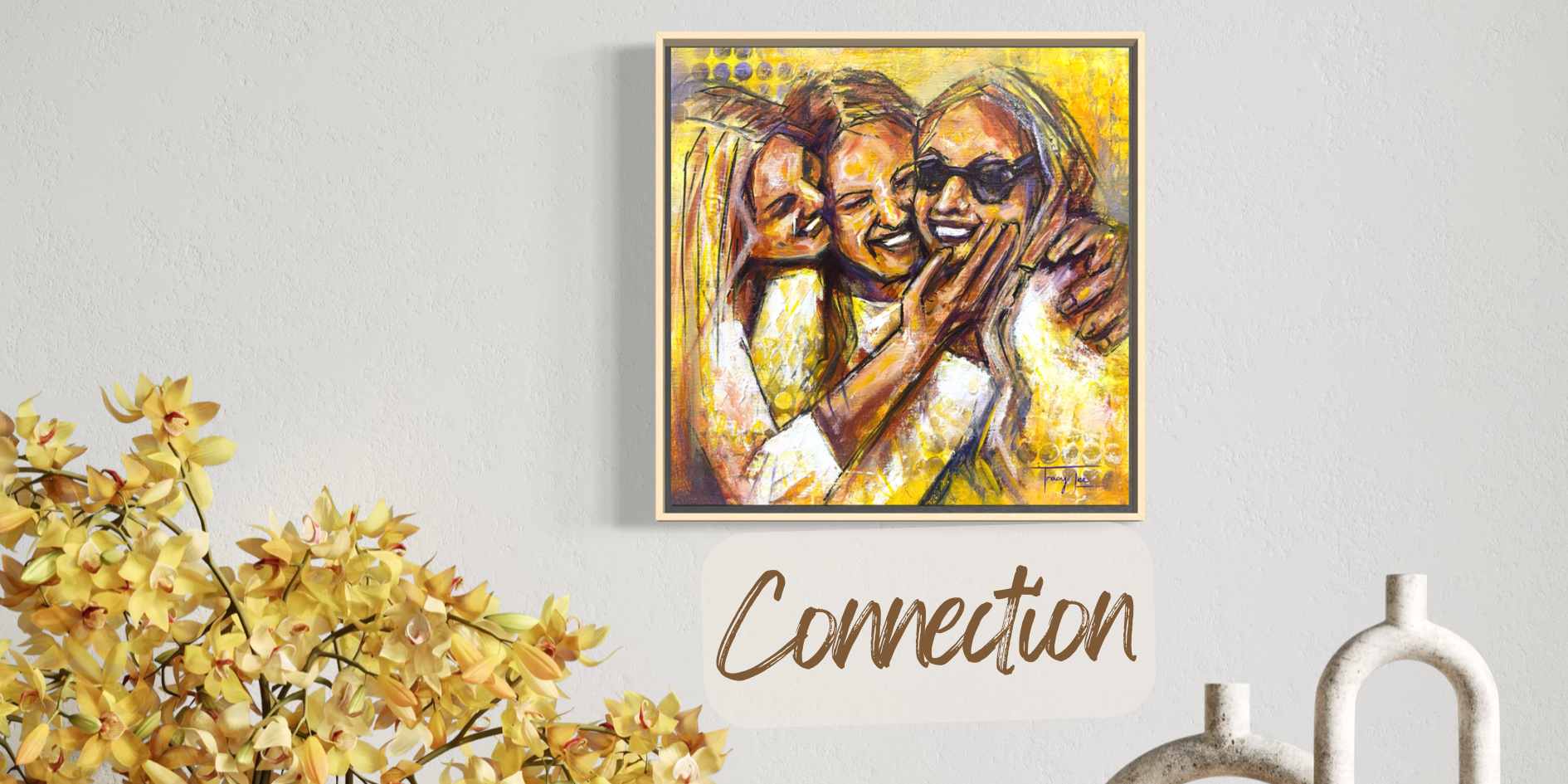 A framed custom portrait painting of three women hugging, displayed on a light gray wall above a decorative white sign that reads 'Connection'. Yellow flowers and a white vase are visible in the foreground.
