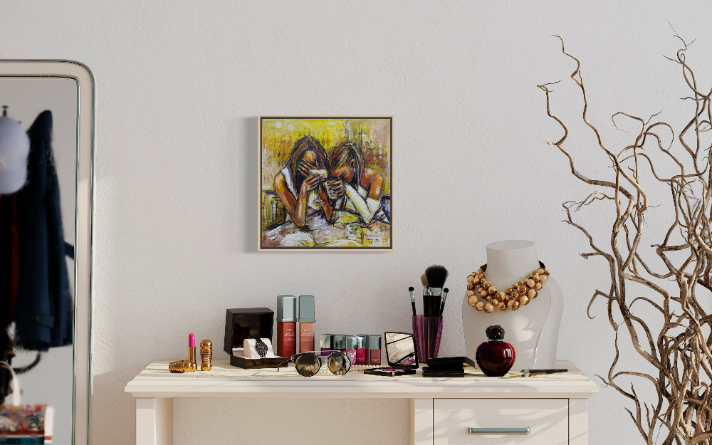 A framed square painting depicting two women laughing, hung on a white wall above a styled white vanity table with cosmetics, brushes, and a gold necklace bust. A large mirror is visible on the left, and decorative branches stand on the right.