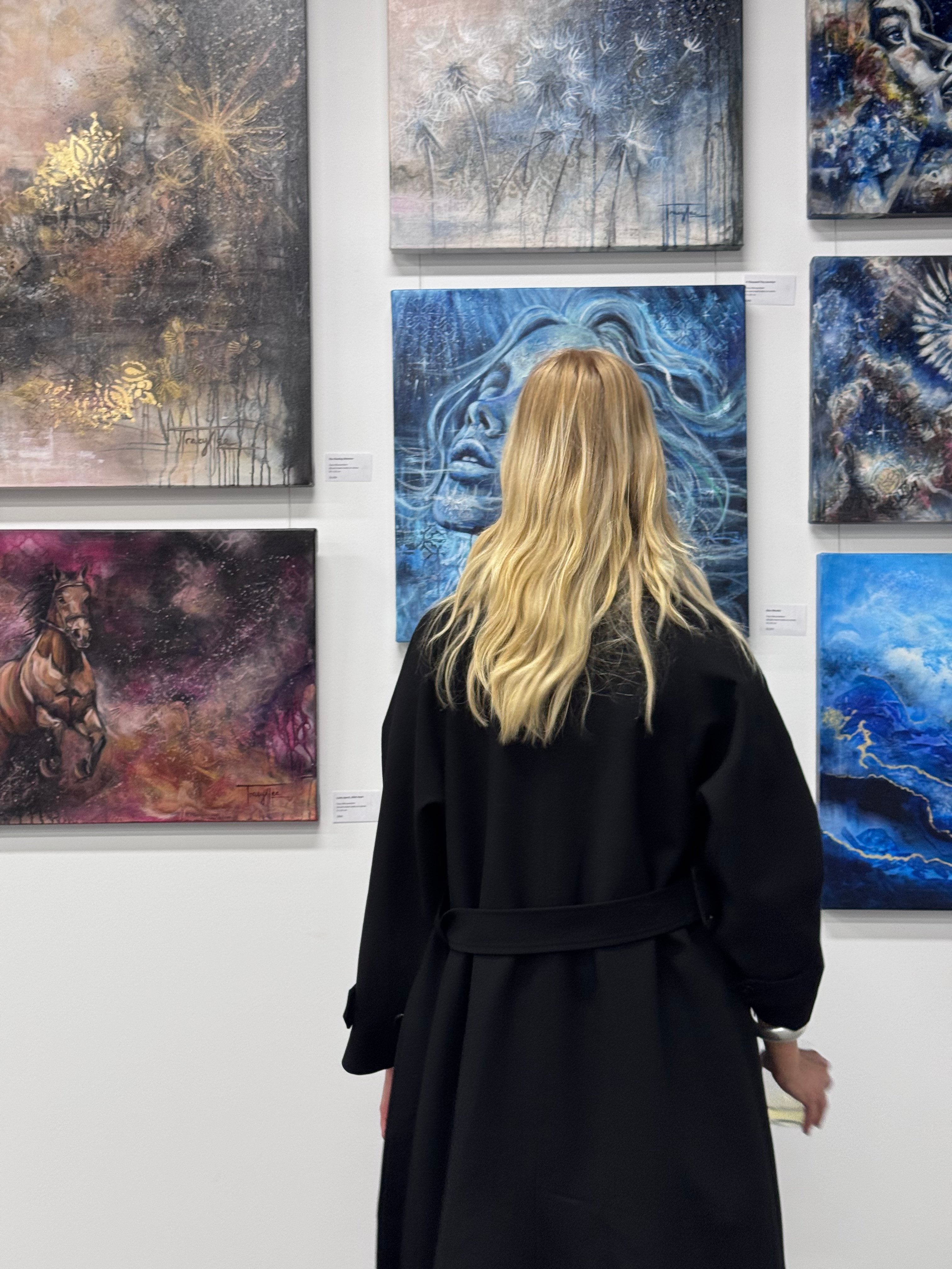 Person in a black coat looking at abstract paintings on a wall