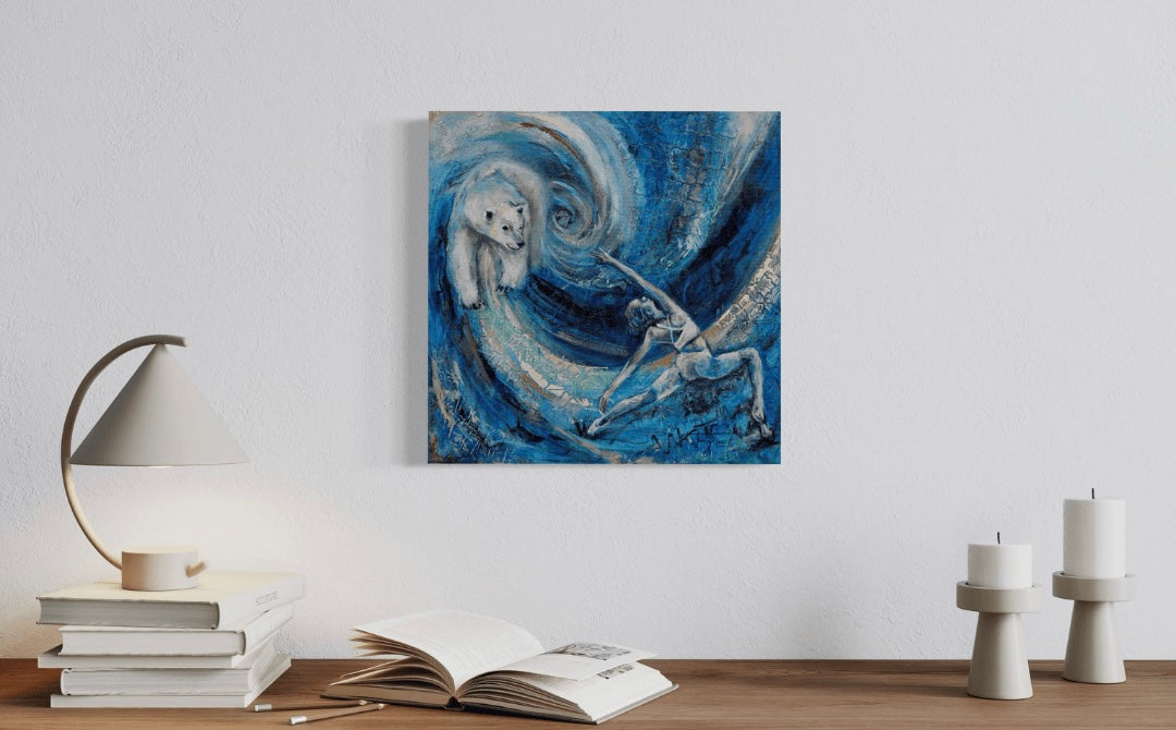 A painting featuring a stylized depiction of a woman and a polar bear against a blue background with swirling patterns. The woman appears to be in a warrior pose, and the polar bear is facing her. The painting is featured in a modern desk scene with candles, table lamp and books.