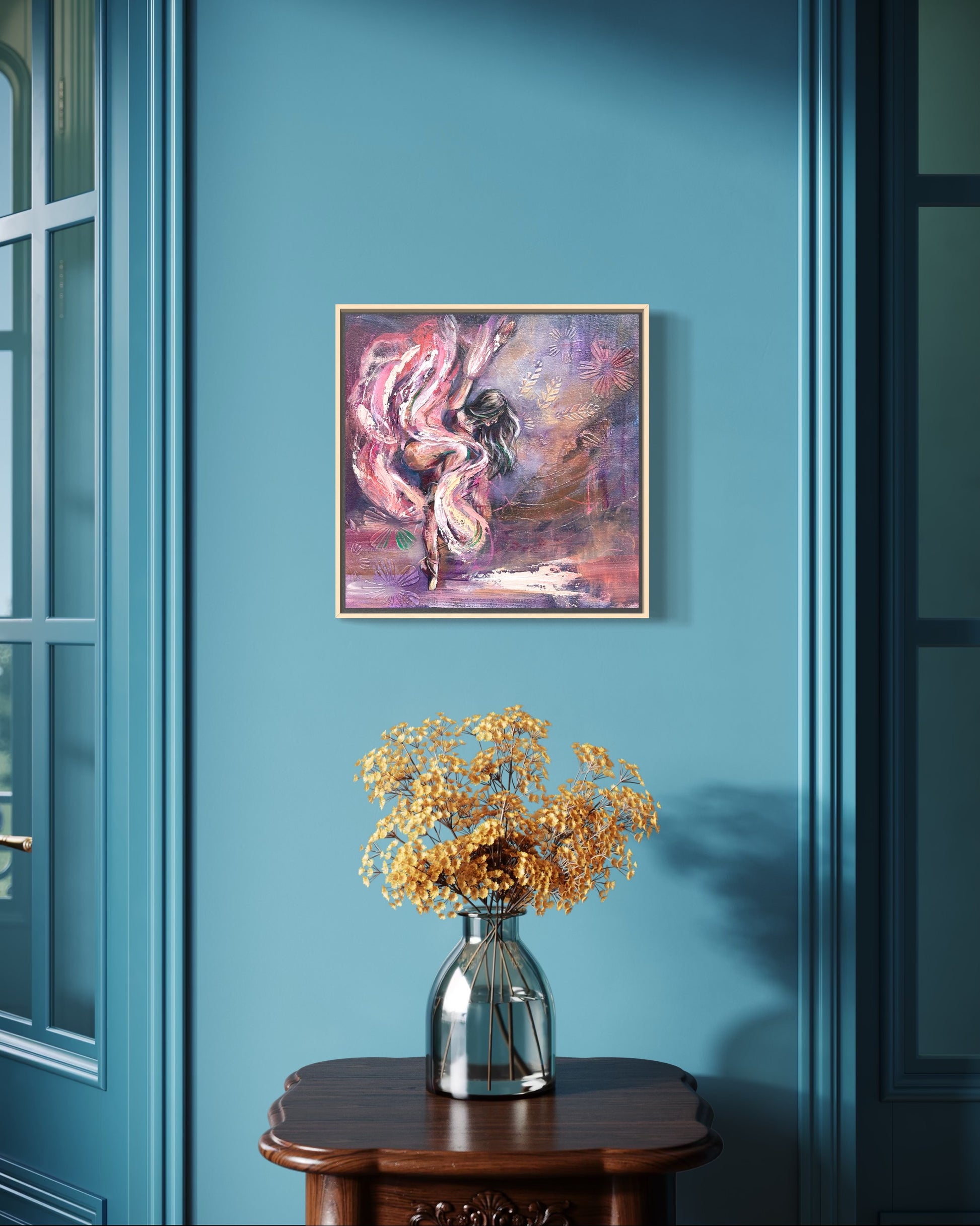 Abstract painting of a ballet dancer in purples and pinks on a blue wall above a vase with flowers on a wooden table.