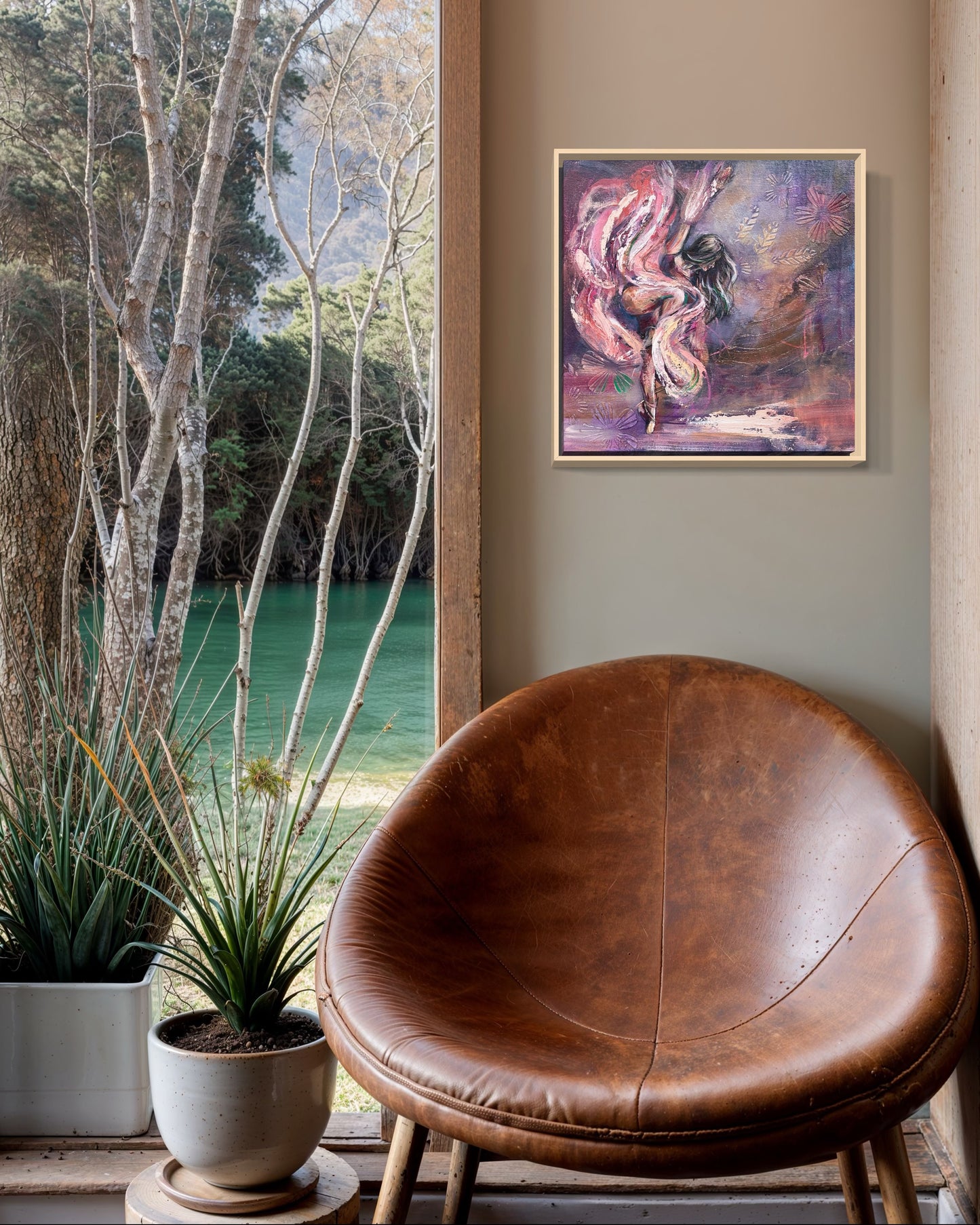 Brown leather chair in a room with a purple and pink dancer painting on the wall and a view of trees and water outside. 