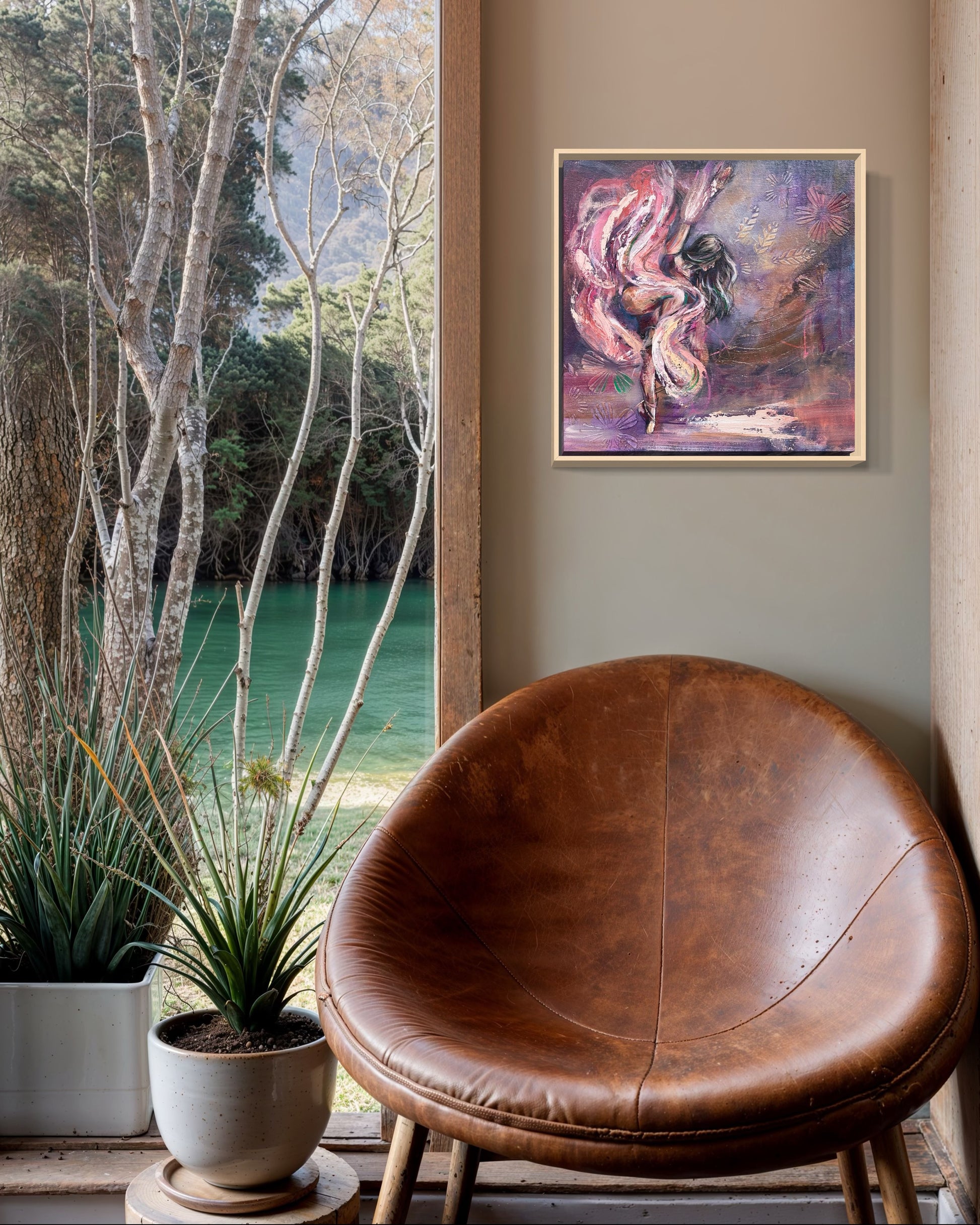 Brown leather chair in a room with a purple and pink dancer painting on the wall and a view of trees and water outside. 