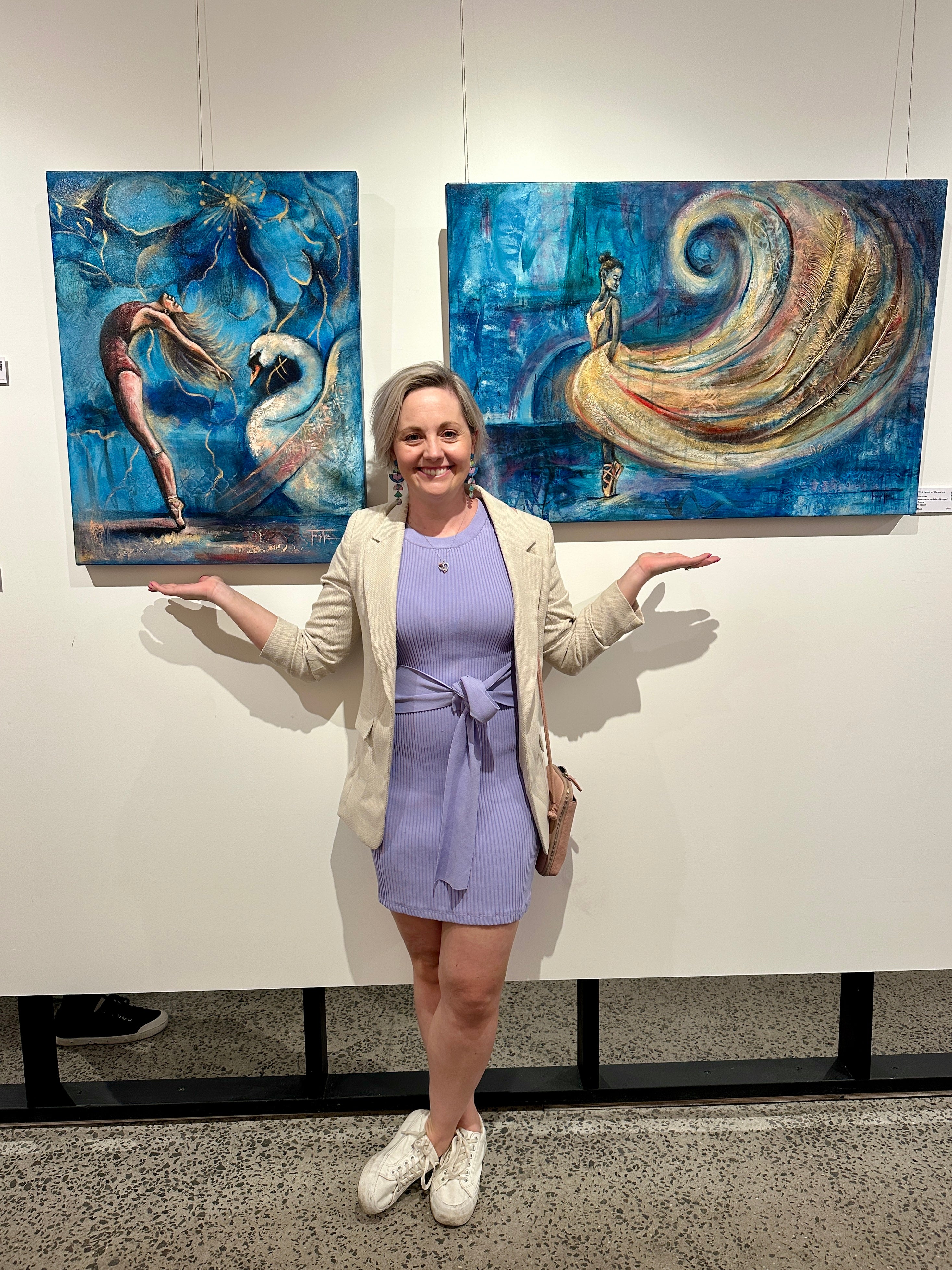 Mixed media Melbourne artist Tracy Lee stands in a purple dress and white shoes and blazer in front of two dancer paintings 